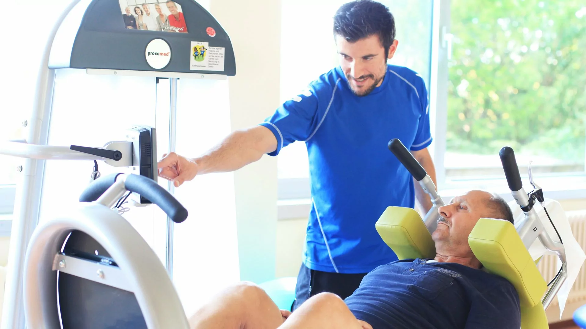 Therapeut zeigt einen Patienten am Fitnessgerät Übungen