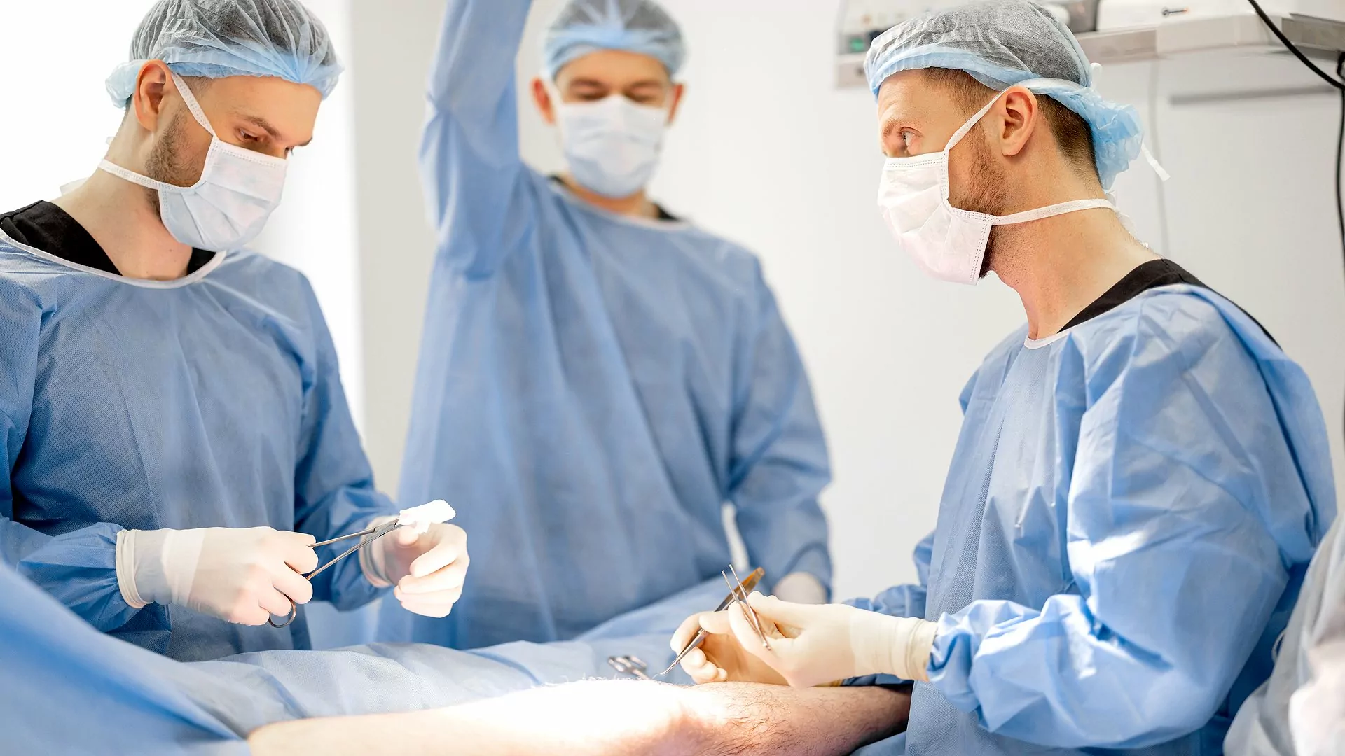 Drei Chirurgen, welche im Krankenhaus eine Knie-Operation durchführen.